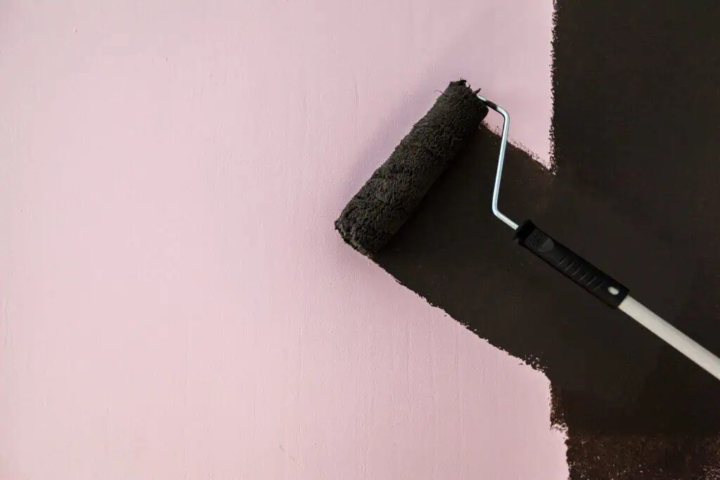Painter applying black paint on pink wall with roller.