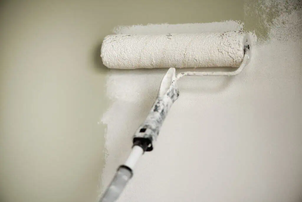 Painter using roller to paint interior wall in a home or office.