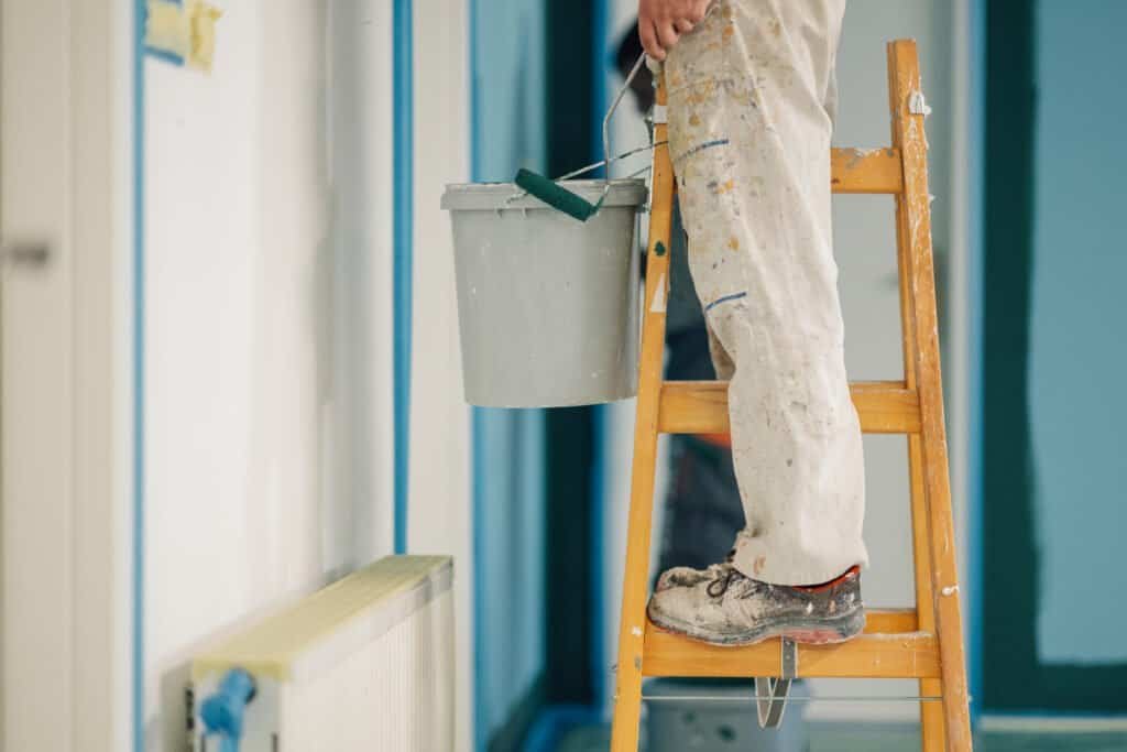Painter on ladder applying paint to interior wall in home.