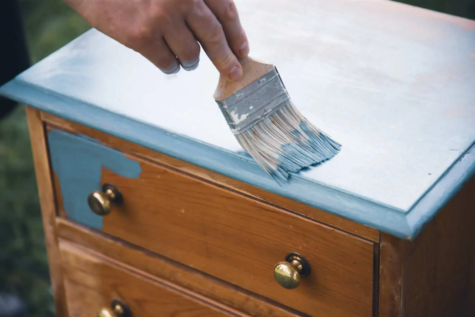 Person applying light blue paint to wooden furniture with a brush.