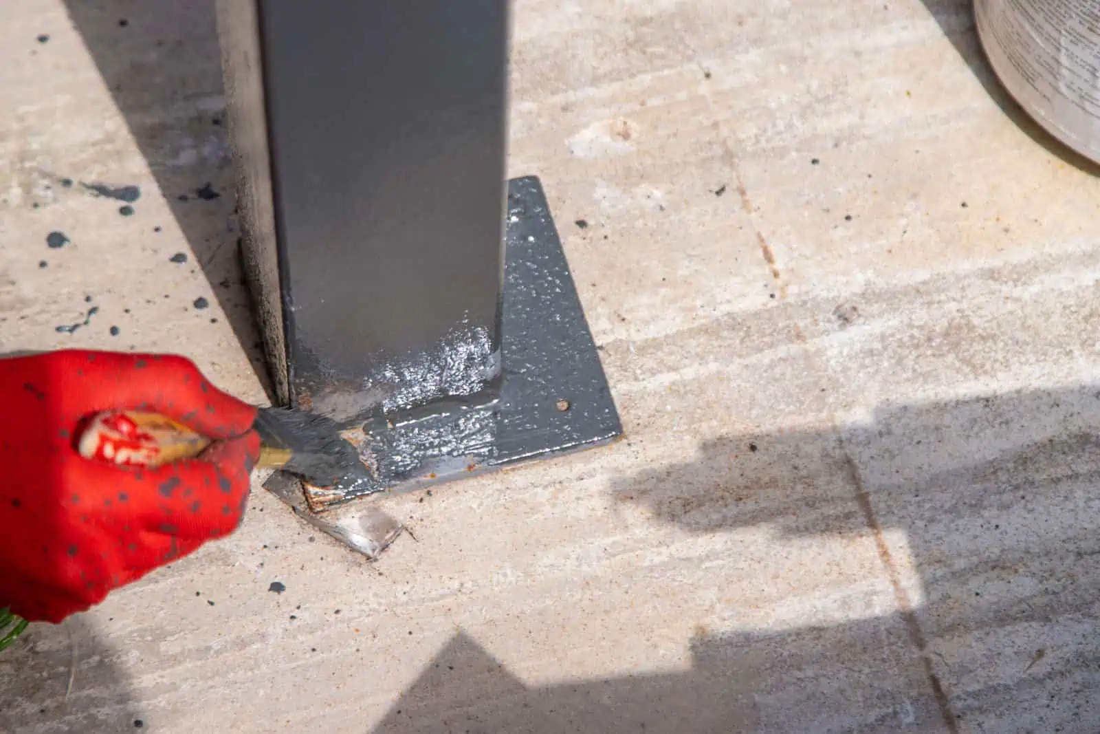 Worker applying protective coating to metal post on concrete surface.